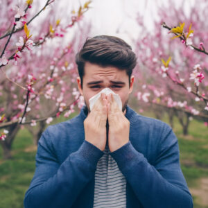Hombre joven estornudando como representación de síntomas alérgicos en el Test ALEX2